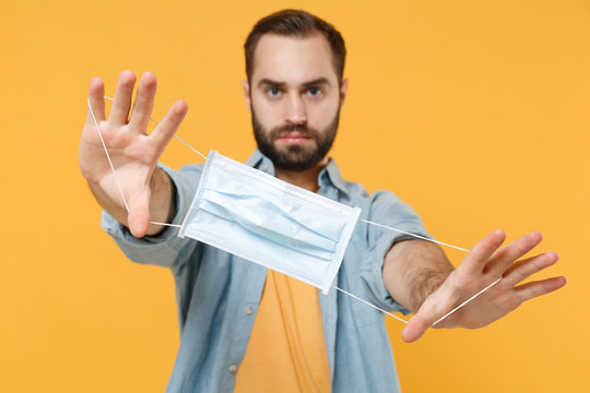Young man in casual clothes posing isolated on yellow background studio portrait. Epidemic pandemic rapidly spreading coronavirus 2019-ncov sars covid-19 flu virus concept. Hold sterile face mask.