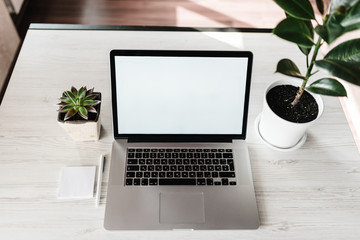 Mockup laptop computer with blank white screen, pen, notes on wooden table. Home interior, office background. Front, top view desktop, workplace. Technology concept. copy space.