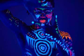 luminous portrait of young man in the UV rays on dark background, fluorescent prints on shirtless...