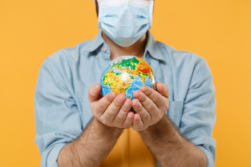 Cropped image of young man in sterile face mask posing isolated on yellow background studio portrait. Epidemic pandemic coronavirus 2019-ncov sars covid-19 flu virus concept. Hold Earth world globe.