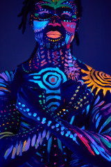 young handsome african man with fluorescent prints on body glowing on neon lights, colorful prints, body art concept