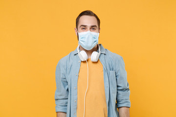 Cheerful young man in sterile face mask with headphones posing isolated on yellow background studio...