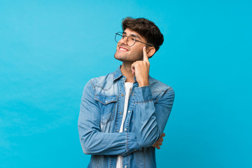 Young handsome man over isolated blue background with glasses