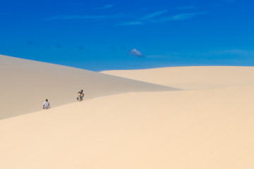 People walk along the sand dunes, view from the back, blue sky