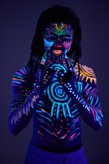 luminous portrait of young man in the UV rays on dark background, fluorescent prints on shirtless body, unusual cosmic mysterious paints