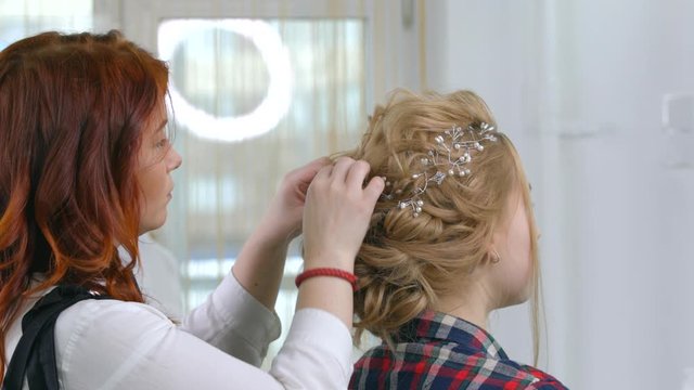 Fastening the hair with tiaras, a make-up master attaches a caron of branches to the hairstyle. Beauty industry, hair care, preparation for the celebration.