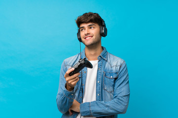 Young handsome man over isolated blue background playing at videogames
