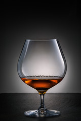 Glass of cognac on the black stone table with radial gradient light background.