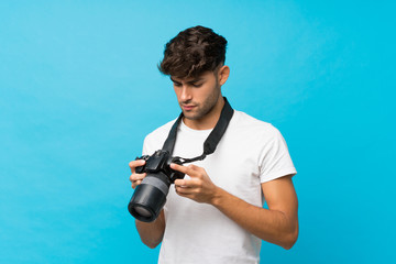 Young handsome man over isolated blue background with a professional camera