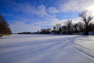 A general plan of a view of a snowy lake with long shadows from the trees.