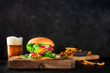 Burger and beer. Hamburger with beef, cheese, onion, tomato, and green salad, a side view on a dark...