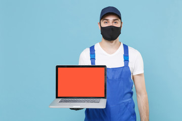 Delivery man in cap t-shirt uniform sterile mask gloves isolated on blue background studio. Guy employee courier hold laptop pc computer Service quarantine coronavirus virus covid-19 2019-ncov concept