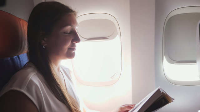 business woman with brown hair wearing grey t-shirt reads book in liner passenger cabin close-up