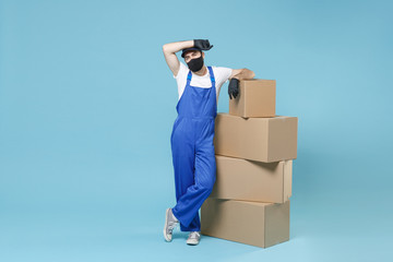 Full length delivery man in cap t-shirt uniform sterile face mask gloves isolated on blue background studio Guy employee courier hold box Service pandemic coronavirus virus covid-19 2019-ncov concept.