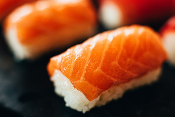 Salmon sushi nigiri in chopsticks over black background