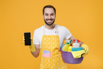 Smiling man househusband in rubber gloves hold basin detergent bottles washing cleansers doing...