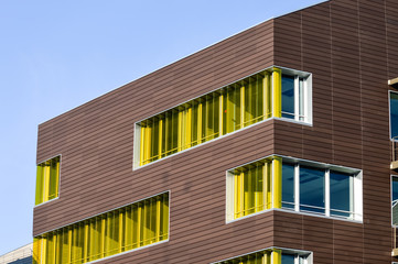 Colorful yellow windows in a modern architecture building. Windows shutters are yellow on a dark wood wall with a blue sky.