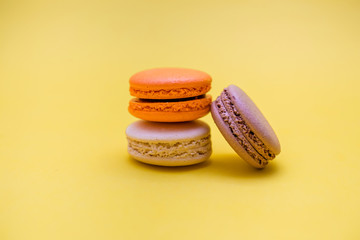 A set of macarons on a yellow background. macarons is orange, cream, brown. Free macarons are stacked in a row. Сopy space.