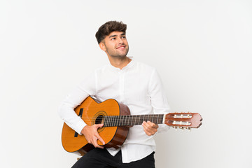 Young handsome man with guitar over isolated white background looking up while smiling