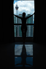 A slender girl is looking at the city through a large window. High floor.