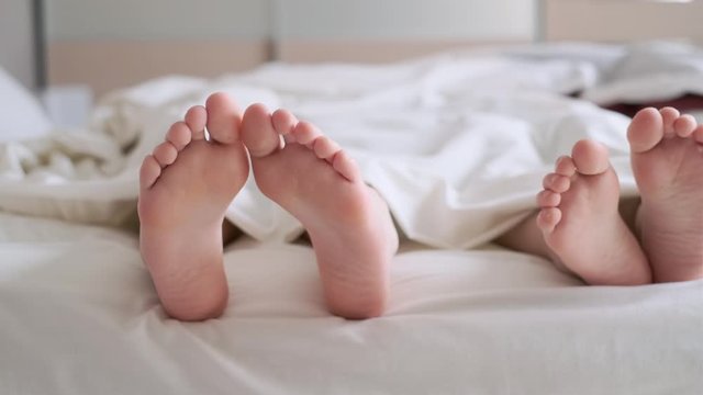 Video of two brothers are lying in a bed and covering with the duvet. Focused on the feets.