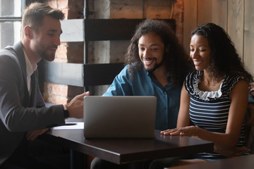 Happy African American couple meet with male consultant in cafe discuss house project on laptop, smiling multiracial man and woman talk with designer or architect wedding planner in coffeehouse