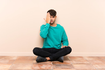 Young handsome man sitting on the floor covering a eye by hand