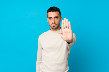 Naklejka premium Young man over isolated blue background making stop gesture