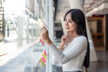 Young asian Businesswoman writing sticky notes on glass wall in office.