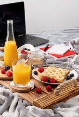 Wooden tray with glass of orange juice and sandwich with berries on the bed