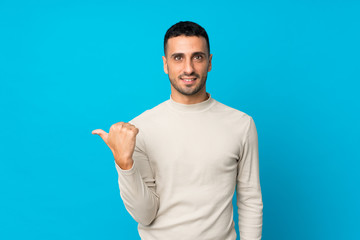 Fototapeta premium Young man over isolated blue background pointing to the side to present a product