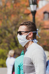 Young man with sunglasses and sewed fabric face mask photographed on the Charles Bridge in Prague, Czech Republic. Blurred people in the background. Travelling, tourism during coronavirus. COVID-19