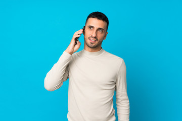 Young man over isolated blue background keeping a conversation with the mobile phone