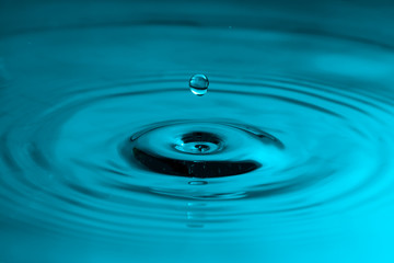 Falling drop of water with ripples in a blue color