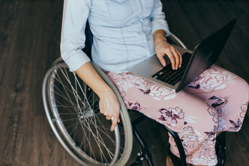 Woman in a wheelchair at home with a laptop on her lap, hand close up, unrecognizable man.