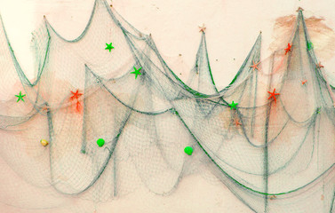 fishing net with bright multi-colored dried starfish hangs on white wall of building. Hobby and fishing concept. Marine vacation backdrop. Selective focus. Copy space.