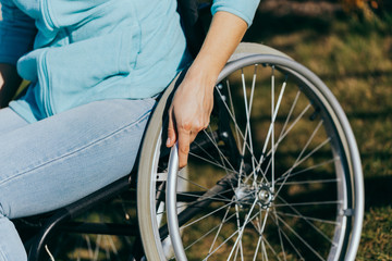 Obraz premium Close up of a young woman in a wheelchair while walking in a park on a sunny day. Recovery and healthcare concepts.