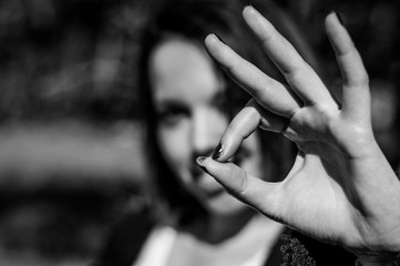 Young woman making ok sign with the hand. Happy girl giving satisfied and supportive hand gesture. Focus on the hand, black and white.