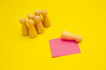 Wooden pawns are stanging over isolated yellow background near pink sticky note for writing. Unemployment concept.