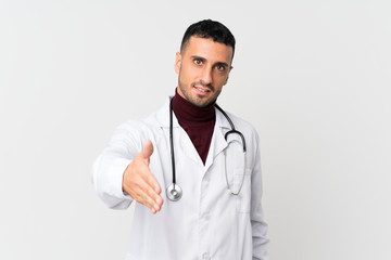 Fototapeta premium Young man over isolated white background with doctor gown and making a deal