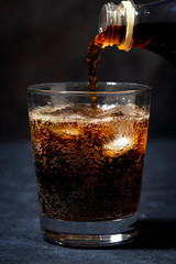 Coca Cola is pouring into a glass from a bottle, closeup vertical