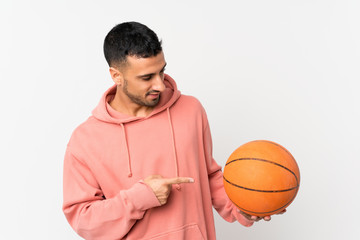 Young man over isolated white background with ball of basketball and pointing it