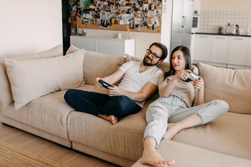 Young couple of man and woman playing video game on a console, sitting on couch in living room.