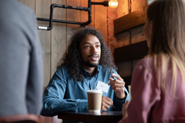 Multiracial young people sit in cafe engaged in speed dating experience chatting and talking, happy diverse multiethnic men and women have fun meeting in coffeehouse for conversation - Powered by Adobe