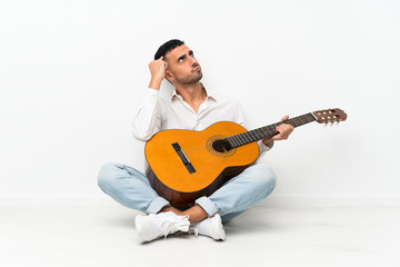 Obraz premium Young man sitting on the floor with guitar having doubts and with confuse face expression