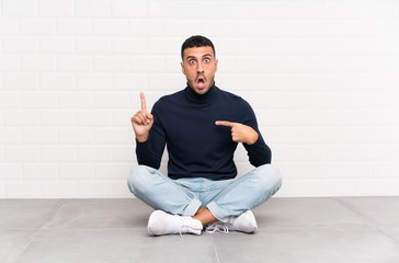 Young handsome man sitting on the floor with surprise facial expression