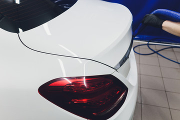 Closeup portrait, young man driver in blue shirt, air drying his silver car with vacuum hose after washing. Safe for expensive paint and chrome. A touch less process that keeps the wax intact.