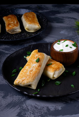 Pancakes with filling are served on the black plate with sour cream and topped with green onion
