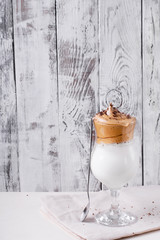 Whipped dalgona coffee in a tall glass against the white wooden background - 343173734