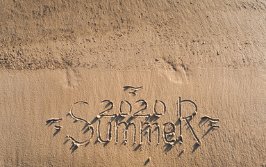 Fototapeta premium The inscription summer 2020 is written on the sand. The drawing is made by hand. Postcard. Beach holidays.